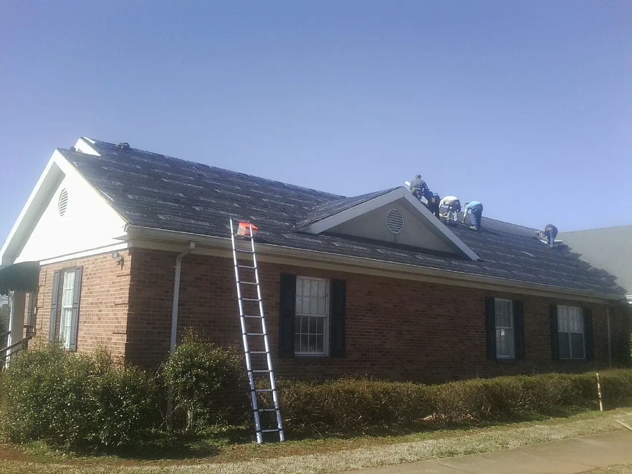 Crew tearing shingles off a brick ranch roof with a ladder set — Emergency Roof Repair work by our crew in Cumberland Foreside