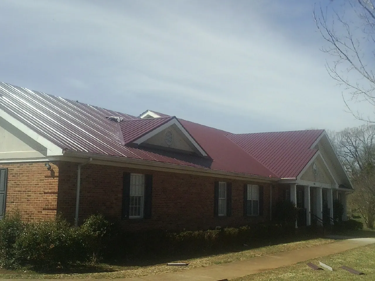 Red metal roof with gabled entries on a long brick building, from a Hail Damage Roof Repair job in Cumberland Foreside