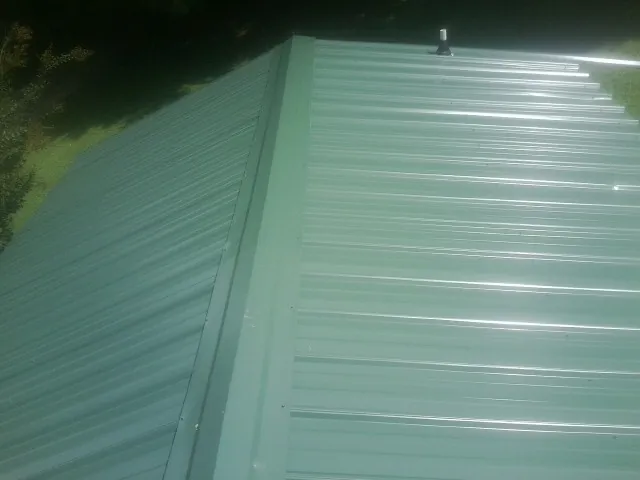 New green metal panels meeting at the ridge of a roof — Flat Roof Repair work by our crew in Cumberland Foreside
