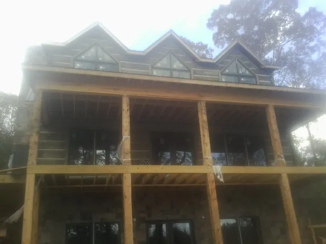 Dormers and porch framing on a large log home under construction — Roof Coating work by our crew in Cumberland Foreside