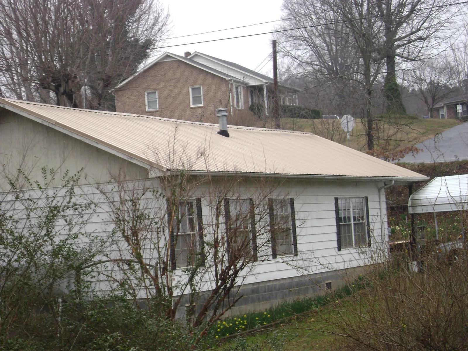 Tan metal roof on a white sided house set into a hillside — Commercial Roofing by Roofing Brothers in Cumberland Foreside
