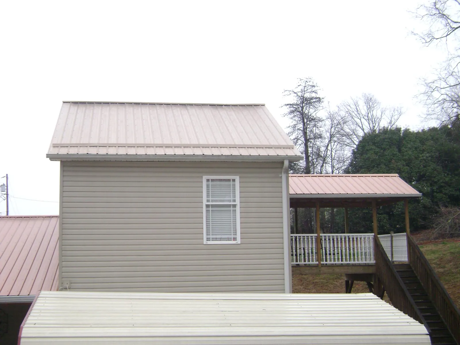 Tan metal roofs on a two story addition and attached porch, from a Roof Replacement job in Cumberland Foreside