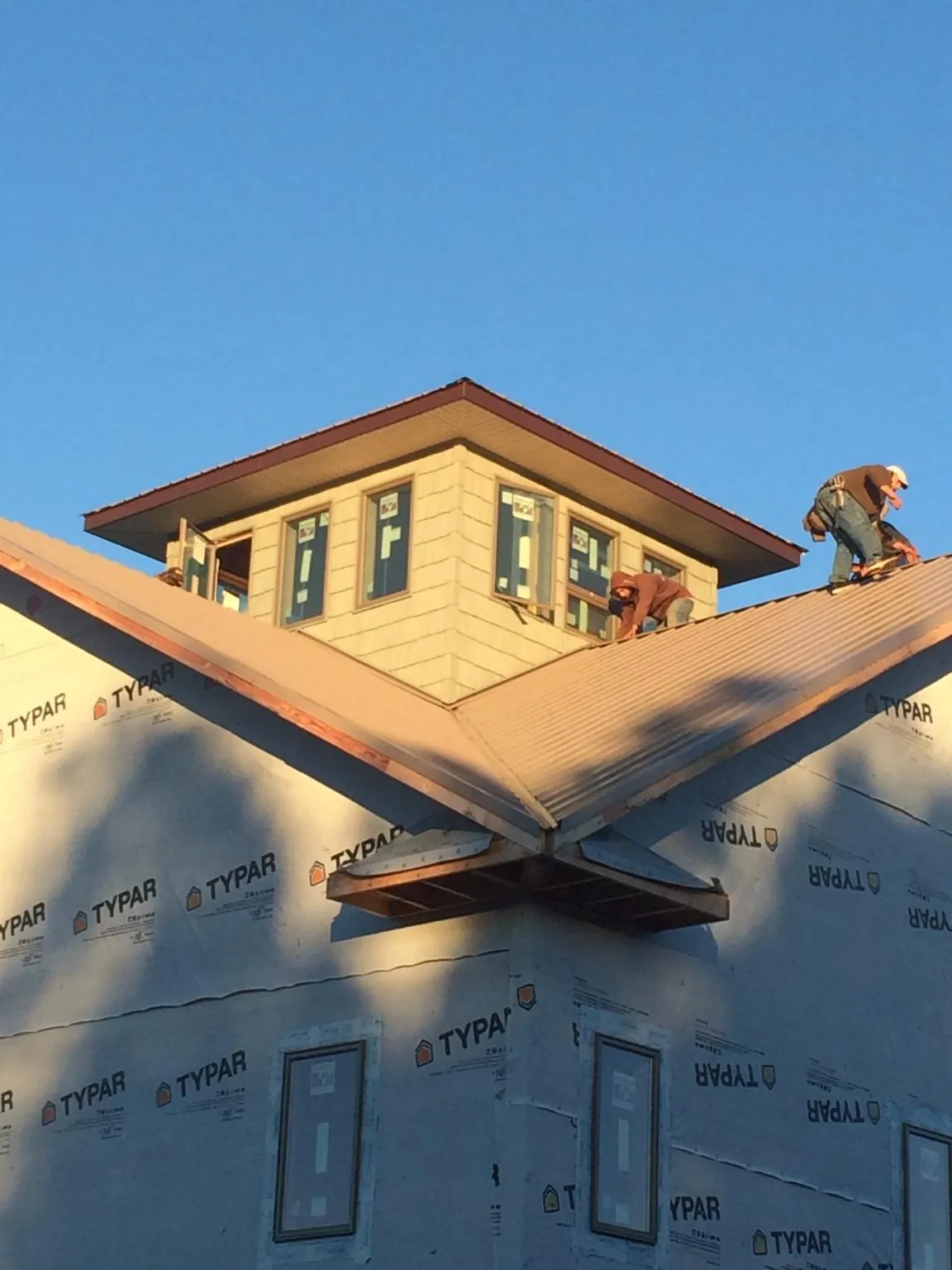 Roofers working around a rooftop cupola on a new metal roof at sunset — Roof Waterproofing in Cumberland Foreside by Roofing Brothers
